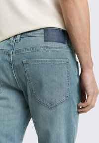 Jasnoniebieskie dżinsy z denimu o strukturalnym kroju, z tylną kieszenią, przeszyciami i ciemną skórzaną naszywką z logo marki.