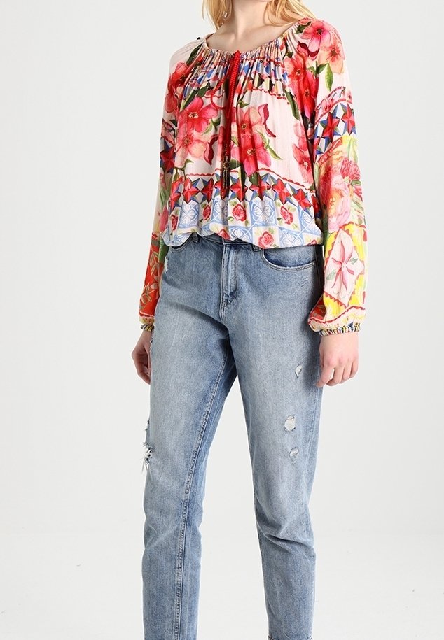 Femme portant un chemisier à manches longues à motifs floraux colorés, assorti à un jean en denim bleu clair usé.