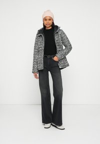 Μπουφάν με μαύρες και λευκές κηλίδες και κουκούλα, συνδυασμένο με μαύρο ριμπ πλεκτό πουλόβερ και σκούρα παντελόνια με φαρδιά μπατζάκια. Ροζ ανοιχτό πλεκτό σκουφάκι.