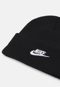 Černá čepice z ribovaného pleteného materiálu, která má ohrnutý lem a vyšitý bílý logo Nike na přední straně.