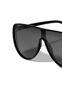 Black oversized sunglasses with a sleek, angular design, dark lenses, and thick frames tapering towards the temples.