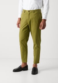 Chinos verts en coton avec une coupe droite, des poches avant et une fermeture à bouton. Associés à des mocassins noirs avec un motif tressé.