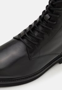 Sorte skinn ankle boot med en glatt overflate, rund tå og klassisk snor-lukking. Diskret sømdetaljer langs siden.