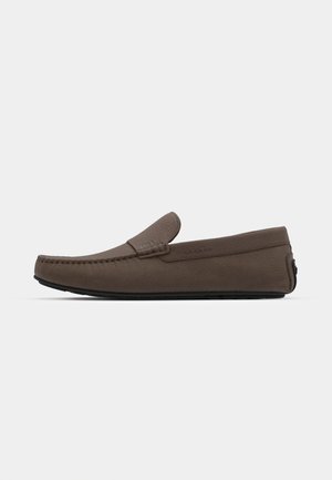 Brown leather loafer with a rounded toe, stitched detailing, and a decorative strap on the vamp. Flat rubber sole. Minimalist design.