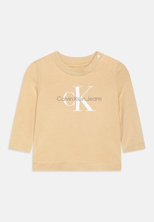 T-shirt beige à manches longues pour bébé avec le logo Calvin Klein Jeans imprimé en blanc et gris sur le devant, avec un bouton pression à l'épaule.