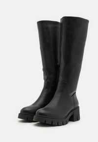 Sorte knelange støvler laget av glatt skinn. Har en grov, teksturert såle og glidelås på siden for enkel påkledning. Elegant design med en robust hæl.