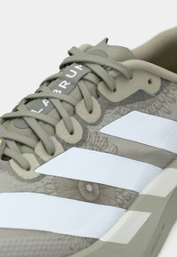 Hall hall spordijalats valgete triipudega, tekstuurse pealismaterjaliga, millel on lillemustrid, ümarate paelte ja tugevdatud silmadega. Reguleeritav keeletapp.