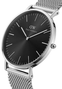 Reloj de esfera negra con correa de malla de acero inoxidable plateado. Presenta un diseño minimalista, índices de hora plateados y una caja de metal pulido.