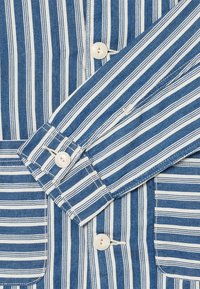 Camicia a righe blu e bianche con colletto button-down, due tasche frontali e bottoni bianchi, con una texture simile al denim.