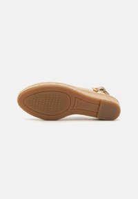 Sandalia beige con un upper de tejido estampado, suela de goma marrón, pequeño tacón y un cierre lateral para ajuste. Texturizada para ofrecer agarre y comodidad.