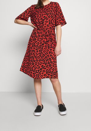 Robe rouge à imprimé léopard avec des manches courtes, détail à la taille nouée et ourlet évasé. Portée avec des baskets noires à enfiler.