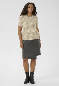 Chemise à manches courtes crème à pois noirs associée à une jupe crayon en denim foncé. Des bottines noires à cheville complètent l'ensemble.