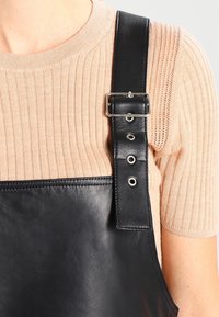 Zwarte leren riem met zilveren gespdetails, bevestigd aan een geribbelde beige stoftop met een gladde textuur en een getailleerd ontwerp.