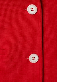 Red textile with a textured surface, featuring two white buttons. The buttons are circular, with a small hole in the center for fastening.