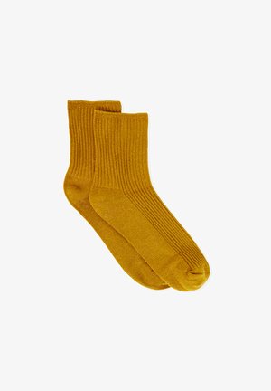 Paire de chaussettes montantes en maille côtelée couleur jaune moutarde, posées à plat sur un fond blanc.