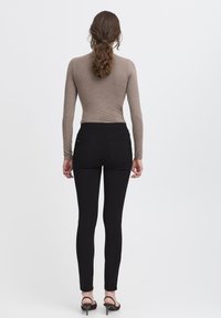 Černé džíny s úzkým střihem, zadními kapsami a hladkým povrchem. Kombinovány s hnědým topem s dlouhým rukávem. Podpatky jsou otevřené a štíhlé.