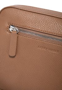 Borsa in pelle marrone con texture, dotata di una zip argentata, un manico in pelle e il logo "GERRY WEBER" impresso. Forma compatta e rettangolare.