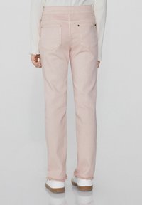 Světle růžové džíny s vysokým pasem, třepeným lemem a dvěma zadními kapsami, kombinované s bílou obuví.