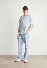 Camicetta a maniche corte di un azzurro chiaro con motivi bianchi a spirale, abbinata a jeans in denim azzurro chiaro e sneaker bianche con suola in gomma.