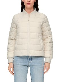 Doudoune beige clair avec un design matelassé, des poignets côtelés et une fermeture éclair sur le devant. Longueur cropped, texture douce et style minimaliste.