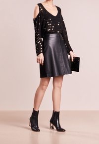 Top nero con paillettes e design a spalle scoperte, abbinato a una gonna A-line in pelle nera. Stivali ankle neri con dettagli metallici sul tacco.