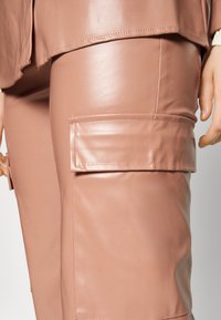 Calças feitas de um impeachment de pele sintética glossy e texturizada numa suave tonalidade de rosa, com um grande bolsos lateral com acabamento suave e design simplificado.