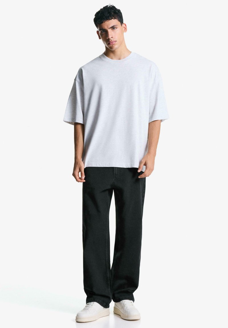 Grå oversized t-shirt med rund halsudskæring, parret med sorte lige ben bukser og hvide sneakers. Glat stoffets struktur, minimalistisk design.
