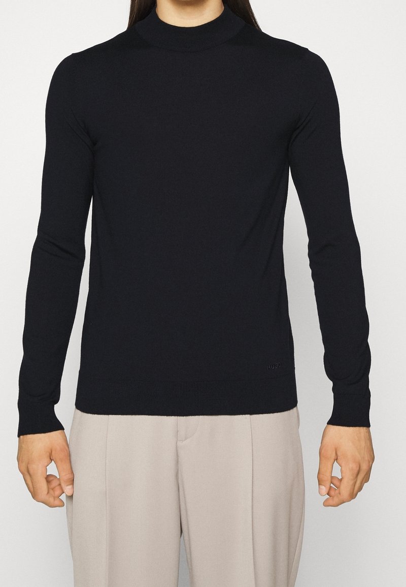 Pull à col roulé à manches longues de couleur bleu marine foncé en matière douce, avec un design ajusté et un ourlet côtelé. Détail de logo discret en bas à gauche.