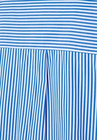 Tessuto a strisce verticali blu e bianche con un design a pieghe. Le strisce variano in larghezza, presentando una superficie liscia e cuciture uniformi.