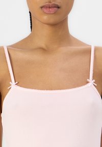 Rosa ribbete tank top med justerbare spaghetti-stropper, med små sløyfer ved stroppe-endene og en teksturert overflate.