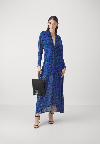 Robe à manches longues avec décolleté plongeant en imprimé floral bleu et violet, tissu fluide, accompagnée d'un sac à main noir avec des détails en frange.