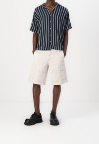 Navyblauw-wit gestreept T-shirt met korte mouwen, beige cargoshorts met zakken en zwarte veterschoenen met dikke zolen.