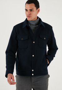 Námornícka vlnená bunda so zmesou materiálov, s golierom, dvomi náprsnými vreckami s klopami, striebornými cvokmi a rovný lem. Nosená cez šedý rolák.