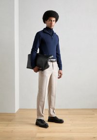 Camiseta de manga larga navy, pantalones beige a medida, cinturón negro y zapatos de cuero negros. Sosteniendo un bolso negro con una textura suave.