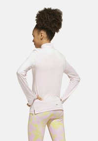 Camicia lunga rosa chiaro con colletto alla coreana, caratterizzata da un orlo dritto e spacchi laterali, abbinata a leggings a fantasia gialli e rosa.