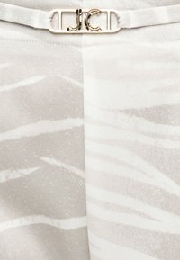 Lys beige stof med subtile abstrakte hvide striber og en guldlås med initialerne "JCD" øverst i midten.