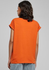 Oranje T-shirt met korte mouwen gemaakt van katoen, met een relaxte pasvorm, opgerolde mouwen en een gladde textuur met een eenvoudig ontwerp.