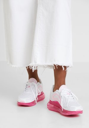 Legs wearing white distressed wide-leg pants and white sneakers with pink accents and thick pink soles on a white floor.