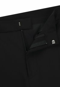 Pantaloni neri su misura con zip nascosta, tessuto liscio, vita piatta e una piccola chiusura metallica sul davanti.