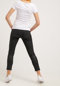 Svarta tight jeans i denim, kombinerad med en tajt vit t-shirt. Elastiskt material med bakfickor och design som slutar vid anklarna.