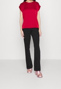 Top corto in raso rosso a maniche corte, pantaloni neri a palazzo e sandali alla piattaforma rosa lucidi. Linee pulite e texture morbide arricchiscono l'outfit.