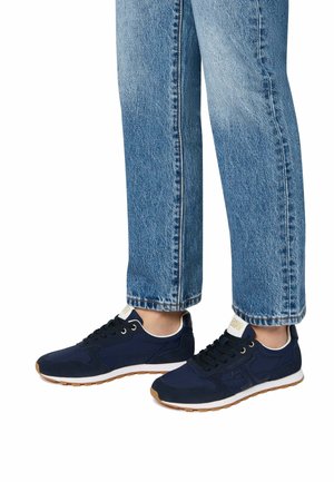Baskets de sport bleu marine en tissu texturé, avec des lacets et une semelle intermédiaire blanche. Associées à un jean droit en denim bleu clair.
