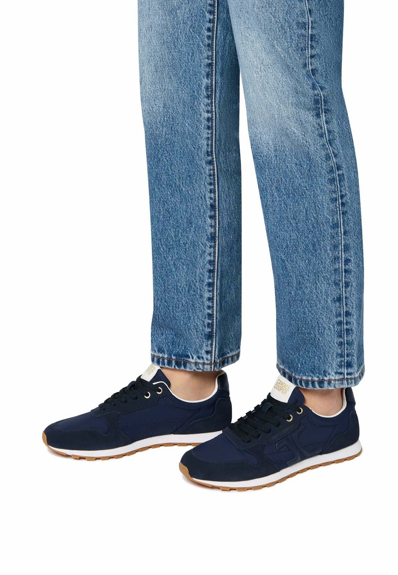Sneakers atletici blu navy con tessuto testurizzato, lacci e una suola intermedia bianca. Abbinati a jeans in denim a gamba dritta blu chiaro.