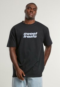 Black cotton t-shirt featuring the text "sweet treats" in light blue. Short sleeves, relaxed fit, plain design, no patterns or embellishments.