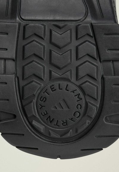 Zwarte rubberen schoenzool met een visgraatpatroon, cirkelvormig logo in het midden en textuurdetails voor grip en duurzaamheid.