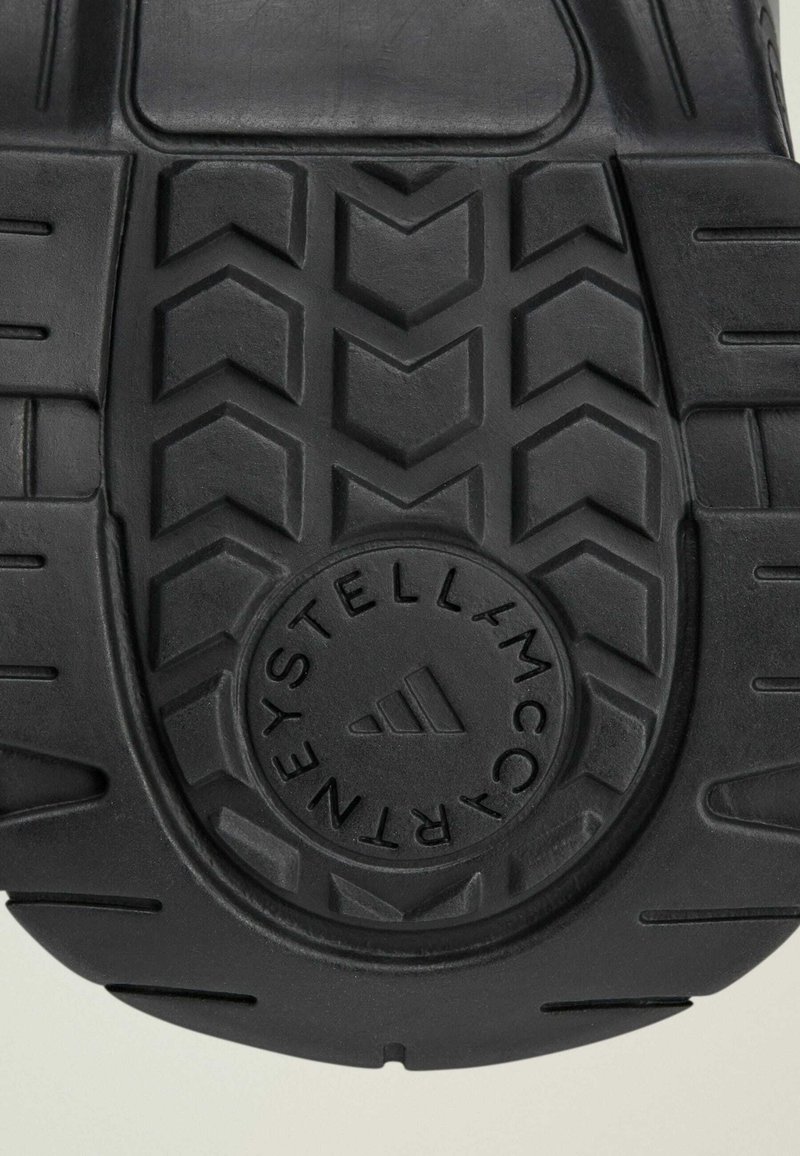 Zwarte rubberen schoenzool met een visgraatpatroon, cirkelvormig logo in het midden en textuurdetails voor grip en duurzaamheid.