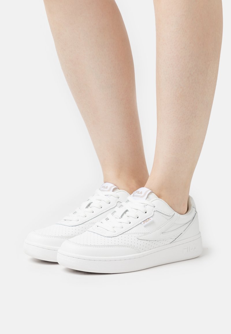 Sneaker bianche con finitura in pelle liscia, dettagli perforati, punta rotonda e suole piatte. Presenta il logo sulla linguetta e sul lato.