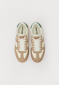 Beige og hvide sneakers med teksturerede accenter, der har et low-top design, hvide snørebånd og en grøn hældetalje. Brandlogo indeni.