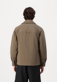 Brown, long-sleeve jacket with a standard collar, buttons on cuffs, and a loop at the back. Smooth texture and relaxed fit.