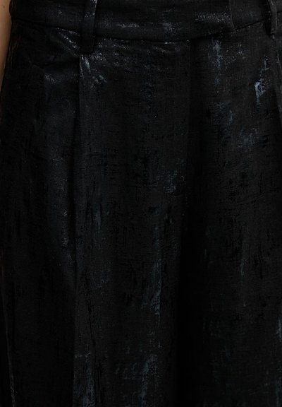 Close-up van zwart gestructureerd stof met subtiele glans op maatwerk kleding, met zicht op tailleband en plooien.